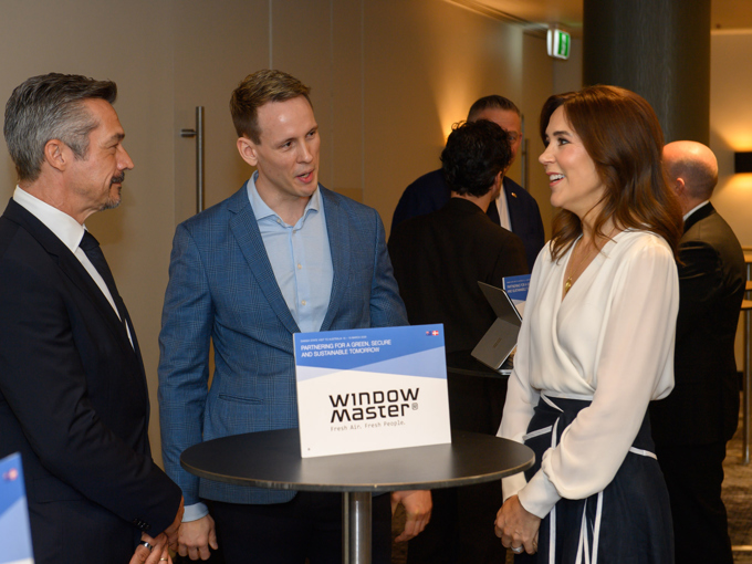 Des personnes en tenue professionnelle discutent debout autour d'une table haute portant l'enseigne « WindowMaster » lors d'une conférence ou d'un événement de réseautage.
