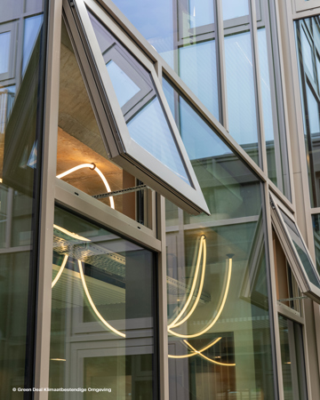 Extérieur d'un bâtiment moderne avec des fenêtres angulaires en verre, certaines ouvertes, reflétant la lumière néon et mettant en valeur un design architectural contemporain.